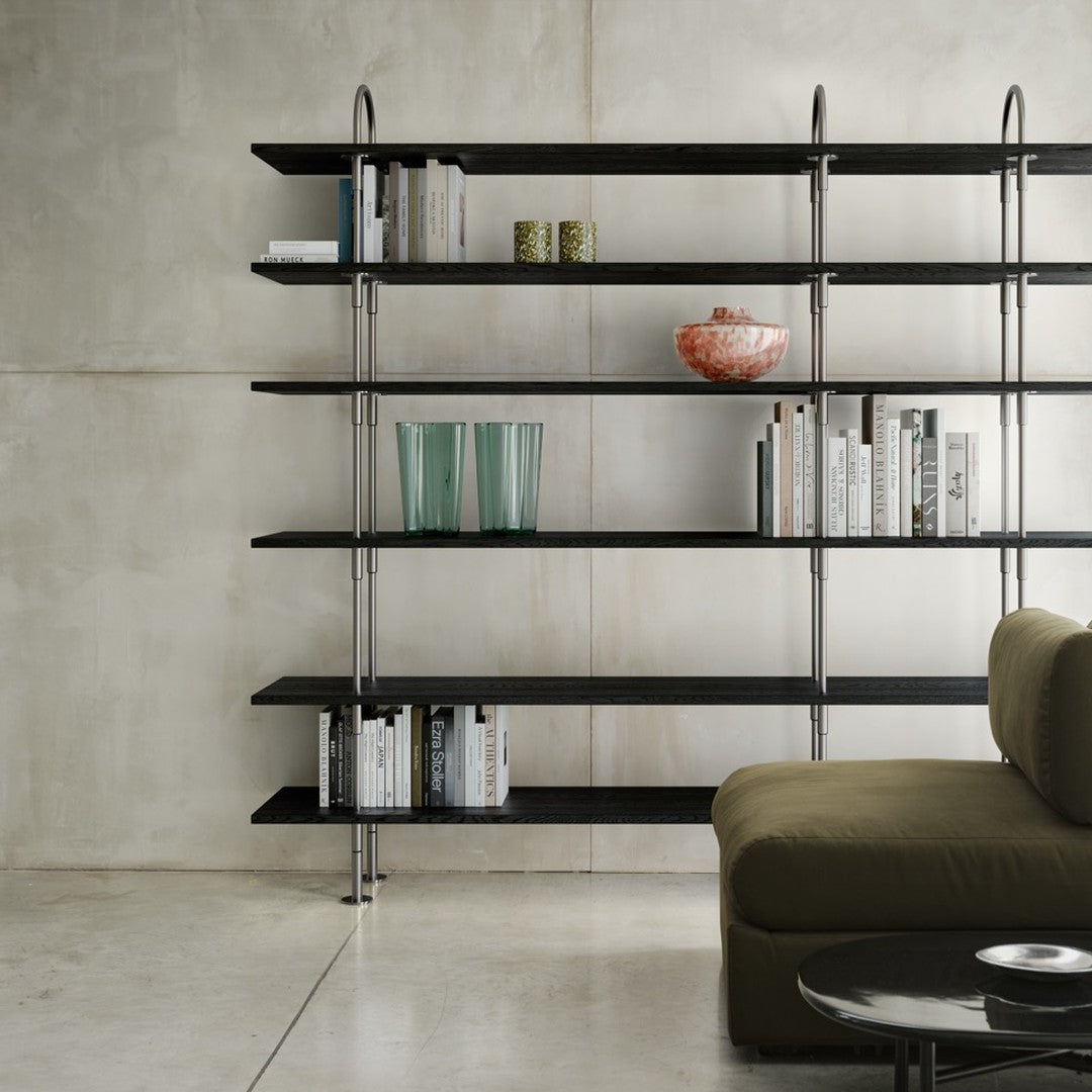 Modern black shelving with metallic accents, transparent green vases, decorative bowl, and earthy olive green sofa.