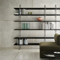 Modern black shelving with metallic accents, transparent green vases, decorative bowl, and earthy olive green sofa.