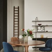 "Wooden ladder, dark shelving, round walnut table, blue and terracotta chairs, and vibrant floral arrangement."