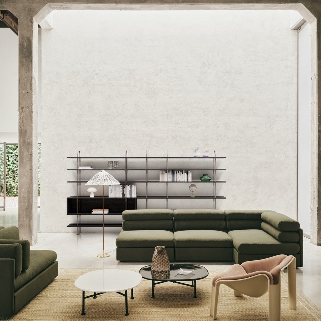 "Modern living room with olive green sofas, black metal shelves, and beige accents, featuring a minimalist, neutral backdrop."
