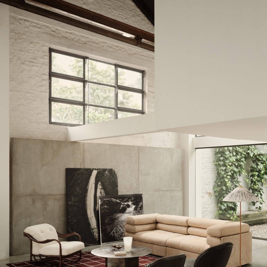 Modern living room featuring beige sofa, black and white artwork, and a red patterned rug against concrete walls.