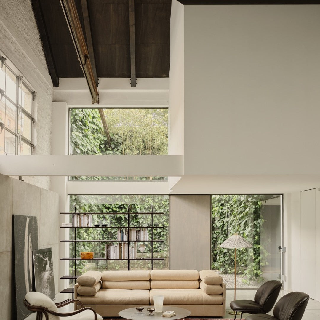Modern living room featuring neutral beige sofa, sleek black chairs, and earthy green foliage accenting large windows.