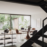 Modern dining room featuring earth tones, sleek black accents, and vibrant green plants against a neutral backdrop.