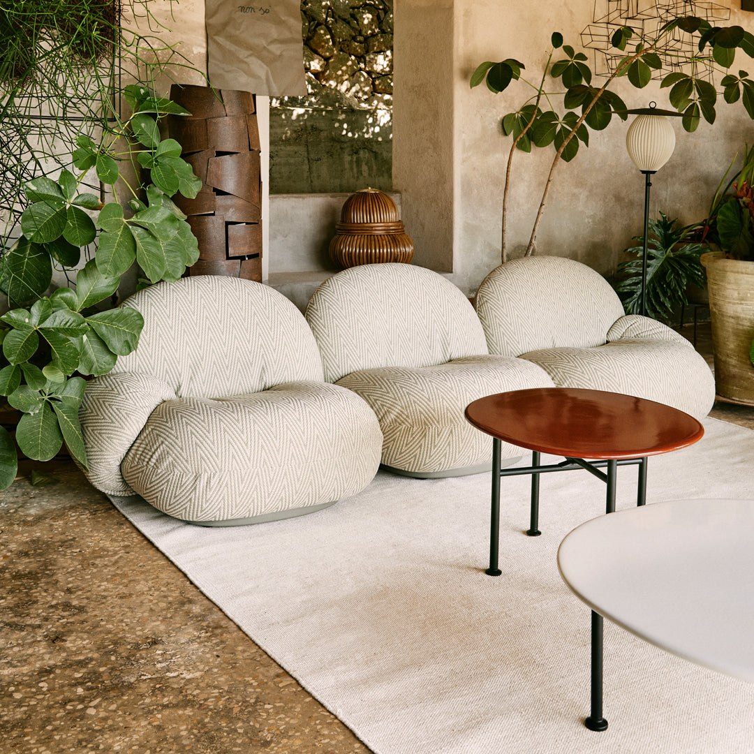 Cream-colored, textured bean bag chairs with a full, rounded shape, set against a natural stone floor and lush greenery.