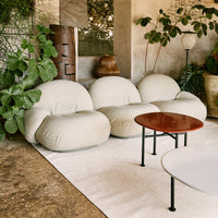 Cream-colored, textured bean bag chairs with a full, rounded shape, set against a natural stone floor and lush greenery.