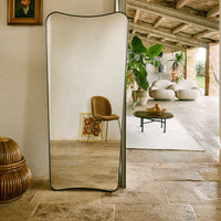 "Curved mirror with a sleek black frame, reflecting earthy tones and a natural interior setting."