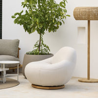 Cozy cream lounge chair with smooth, rounded shape, set against neutral tones and natural greenery.
