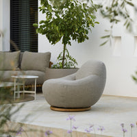 Cozy beige lounge chair with a smooth, rounded shape, set against a modern outdoor backdrop with greenery.