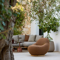 Cozy brown armchair with a smooth texture, complementing gray cushions and earthy tones in a serene outdoor setting.