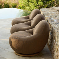 Brown, textured fabric chairs with a smooth, rounded design, placed beside a stone wall and lush greenery.