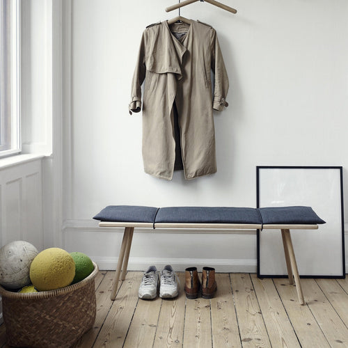 Beige trench coat, navy blue bench with cushions, natural wood legs, and colorful decor balls on a light wooden floor.