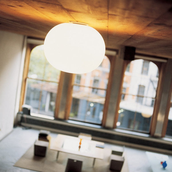 Modern white orb ceiling lamp against a warm wooden ceiling, casting a soft glow in a stylish, minimalist space.