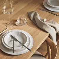 Elegant white dinnerware on a natural wood table, complemented by neutral linen and minimalist glassware.