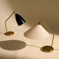 Black and gold modern table lamp alongside a beige conical lampshade with gold accents on a light background.