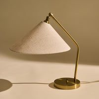 Gold metal lamp base with a beige linen shade, showcasing a modern, minimalist design.
