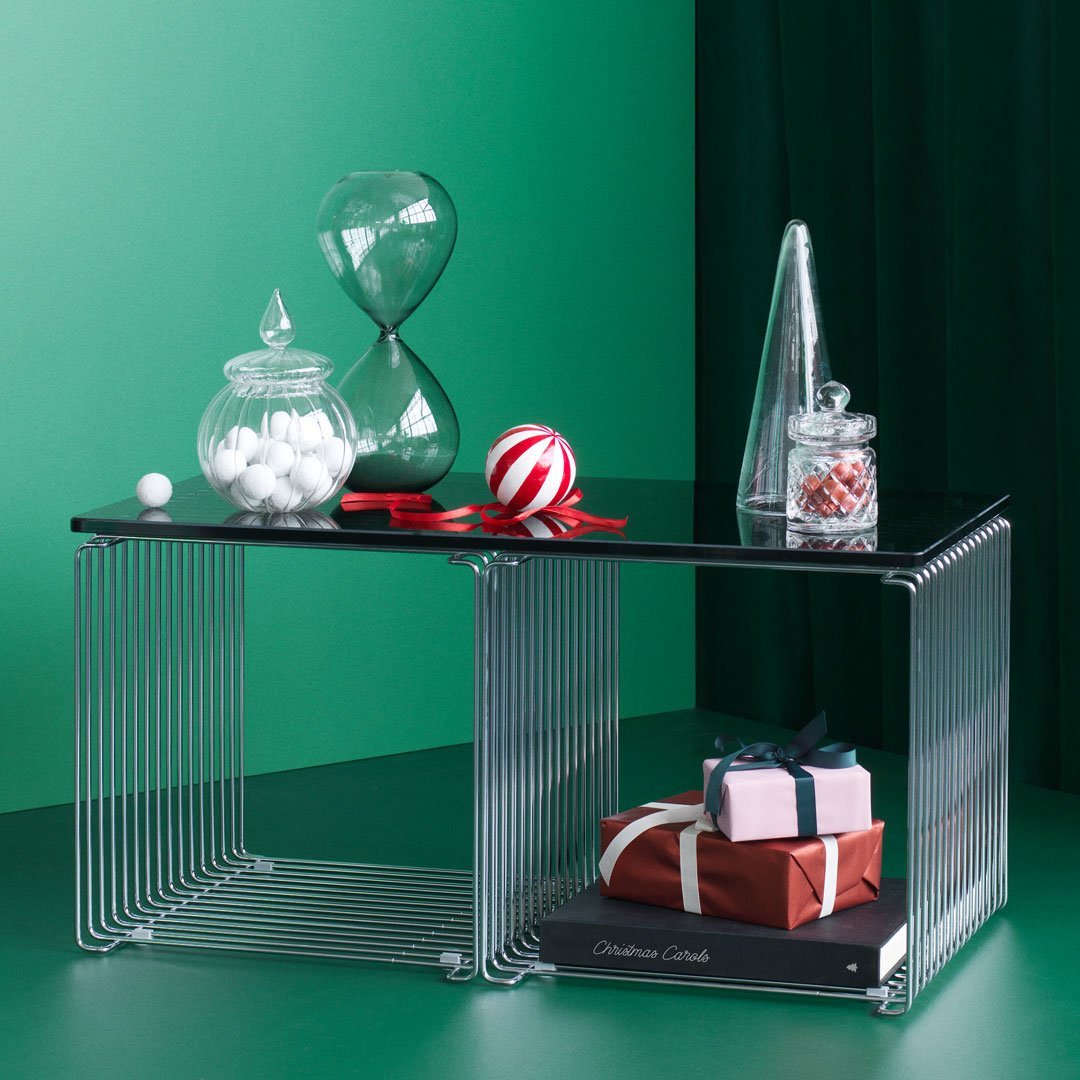 Modern black tabletop with chrome wire base, surrounded by green, white, and red decorative items and gifts.