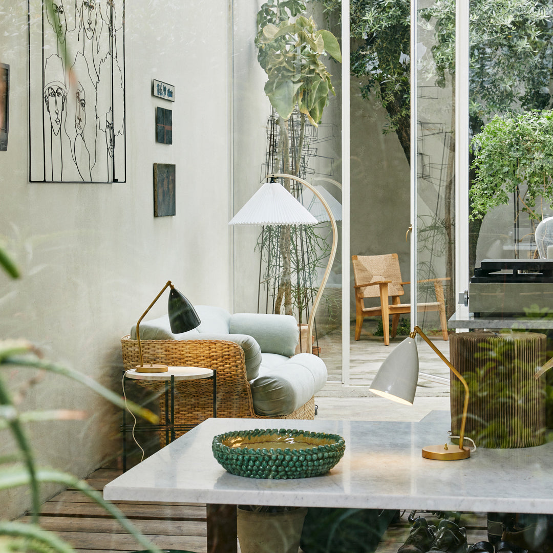 "Light green sofa, natural wicker chair, white and gold lamps, patterned green bowl on a marble table in a modern interior."
