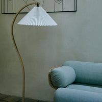 White pleated lampshade with a gold base beside a soft blue couch with a round cushion. Elegant and modern design.