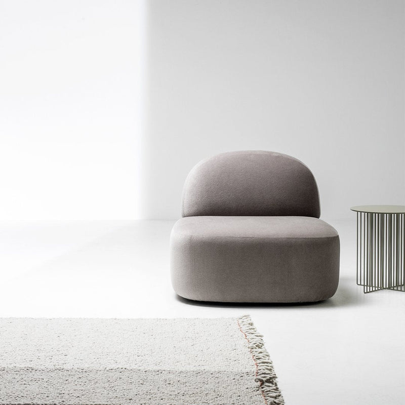Soft gray upholstered chair with smooth curves, paired with a textured white rug and sleek metal side table.