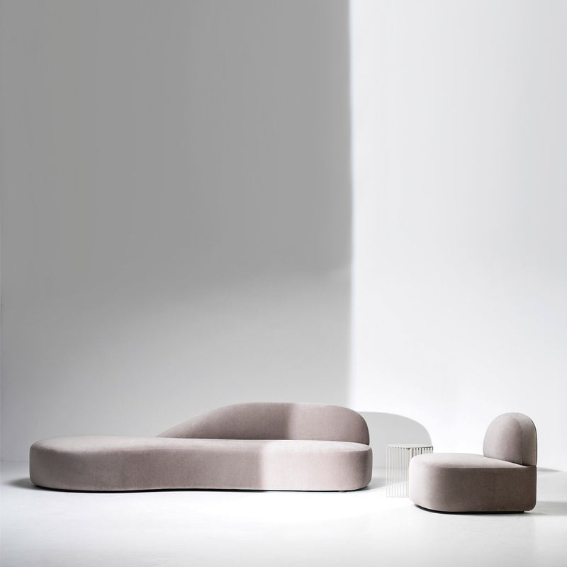 Soft pink curved sofa set against a minimalist white backdrop, featuring sleek and smooth upholstered patterns.
