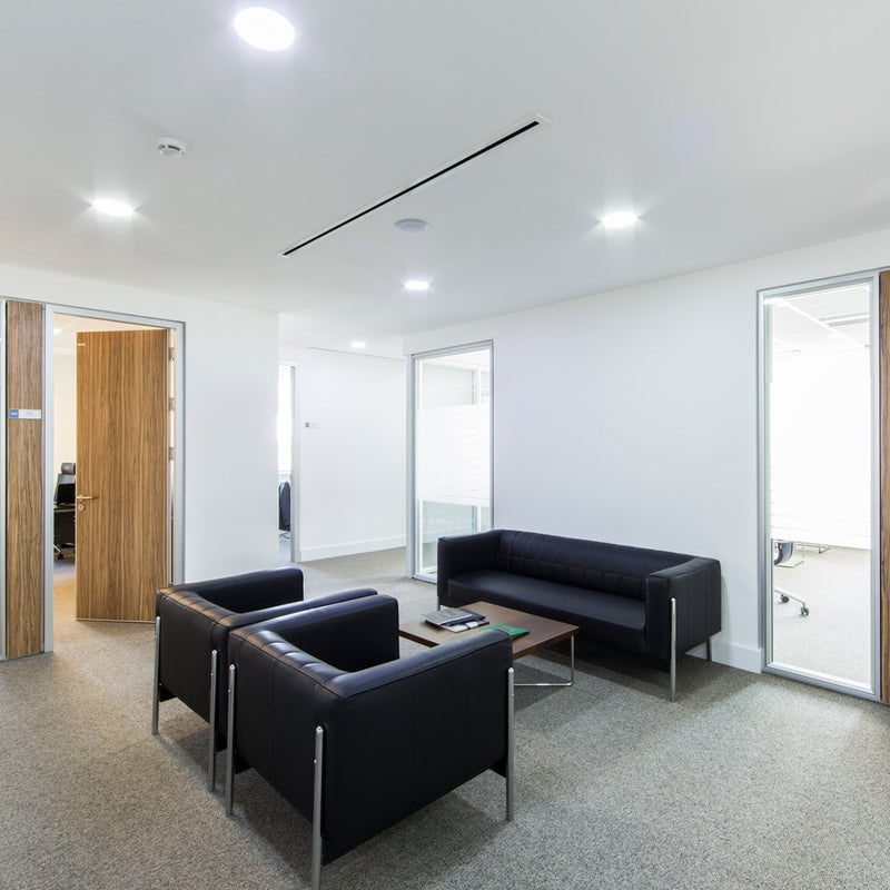 Black leather sofas and wooden accents in a modern, minimalist office setting with neutral carpet and white walls.