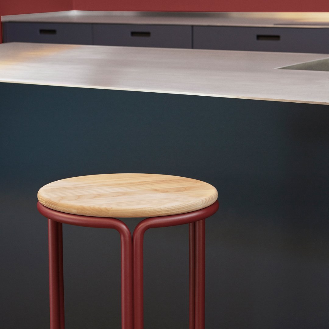 "Modern bar stool with a natural wood seat and sleek red metal legs, set against a darkly colored kitchen backdrop."