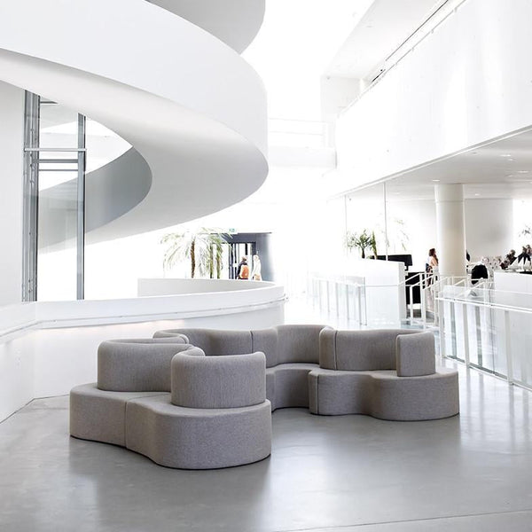 Light gray modular sofa with a smooth, rounded design, set against a bright, minimalist interior.