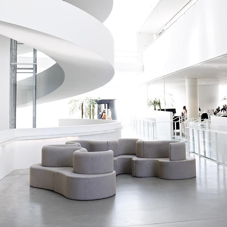 Curved gray modular sofa with a smooth texture, set against a minimalist white interior.