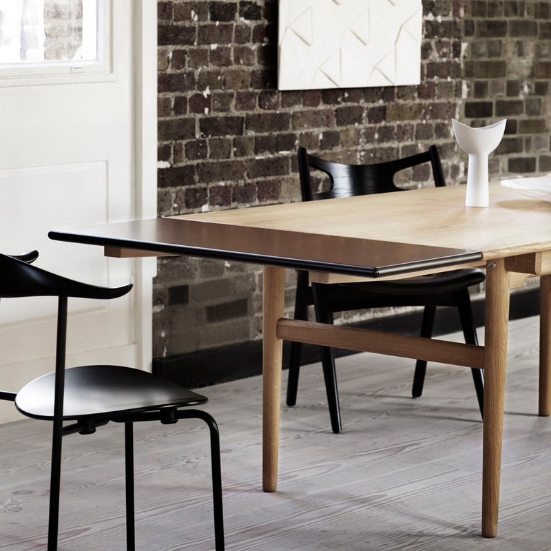 Wooden table with black tabletop, featuring a natural wood finish and minimalistic design, set against a textured brick wall.