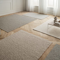 Neutral-toned area rugs in varying textures and patterns on a light wood floor, featuring soft beige and gray shades.