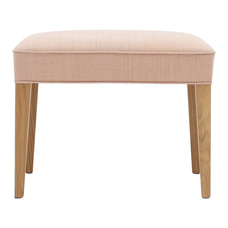 Soft pink upholstered stool with a smooth texture and natural wood legs. Elegant and modern design.