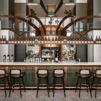 Elegant bar with green tiles, warm wood accents, and a chic herringbone floor pattern, featuring stylish black chairs.