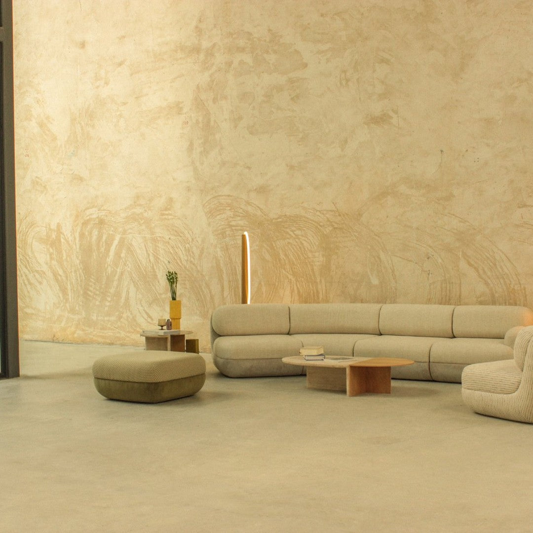 Beige curved sofa with soft texture, complemented by a round olive green ottoman against a minimalist beige wall.