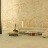 Beige curved sofa with soft texture, complemented by a round olive green ottoman against a minimalist beige wall.