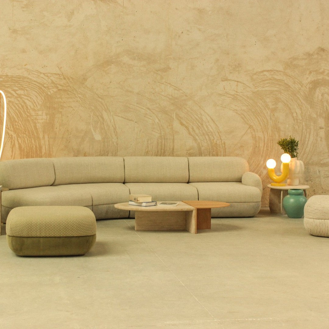 Beige curved sofa with soft textures, paired with green pouf, wooden coffee table, and stylish lamps against a neutral wall.