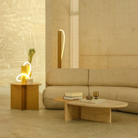 Beige sofa with organic shape, gold accent table, and subtle lighting against a textured light-colored wall.