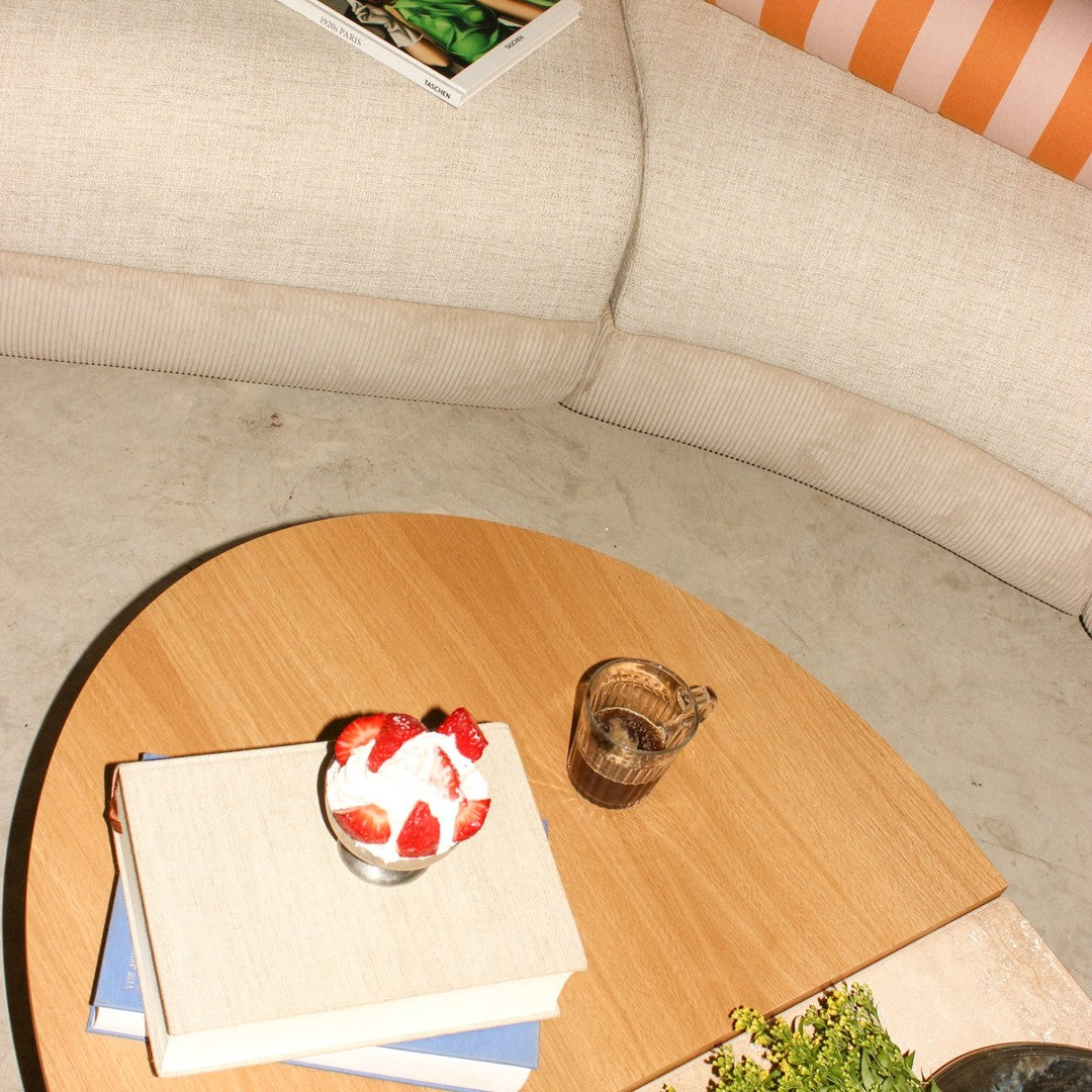 "Round wooden coffee table with a light beige couch, featuring white and orange striped cushions and vibrant decor."