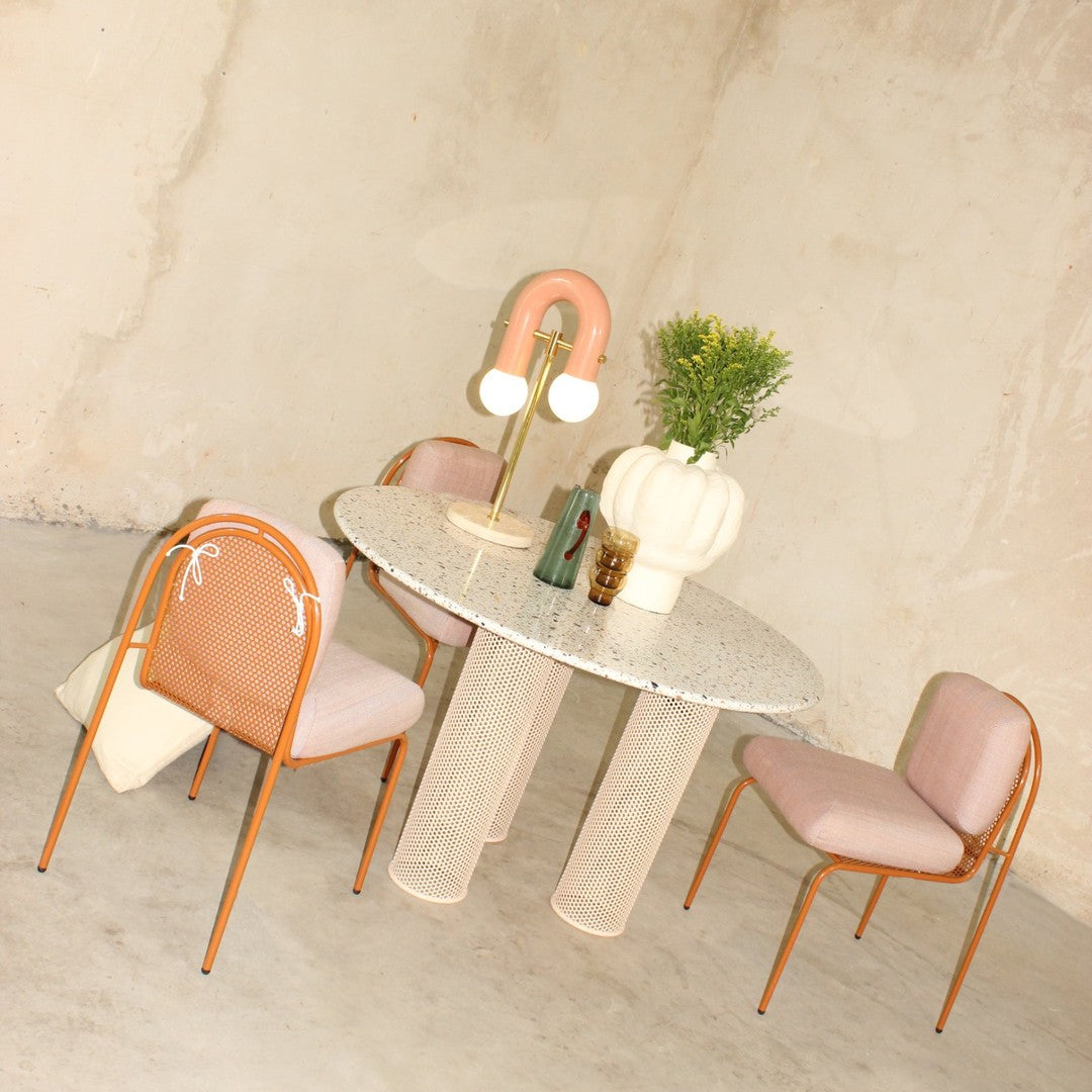 Modern round table with a speckled top and pastel pink chairs, featuring soft curved patterns and earthy tones.