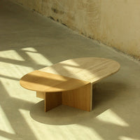 Light wood coffee table with a smooth, oval top and geometric base, featuring neutral tones and a minimalist design.