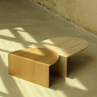 "Two modern coffee tables: one light wood with a smooth finish, the other a matte beige stone, featuring organic shapes."