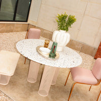 Round terrazzo table with white and black speckles, paired with soft pink chairs and a textured white vase.