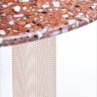 Terrazzo tabletop in warm brown tones with white and black flecks, supported by a light mesh base. 