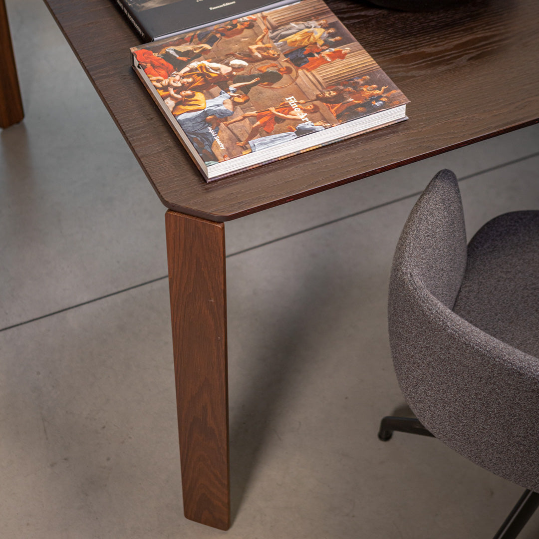 Wooden table with a deep brown finish, paired with a grey upholstered chair. Modern, minimalist design accentuated by sleek lines.