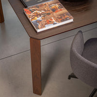 Wooden table with a deep brown finish, paired with a grey upholstered chair. Modern, minimalist design accentuated by sleek lines.