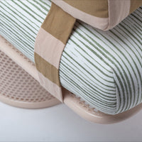 Striped green and white cushion with beige and brown accents on a soft pink base, showcasing modern textile patterns.