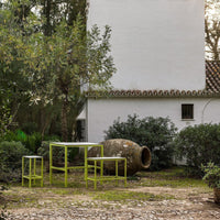 Green outdoor furniture set against a white wall and rustic pottery, blending natural and modern elements.