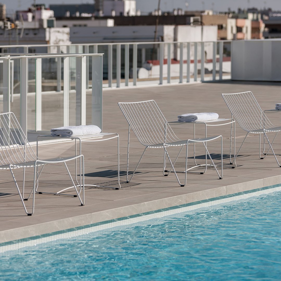 White wire chairs with a sleek modern design by a turquoise poolside, set against a city skyline.