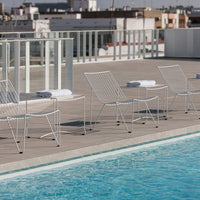White wire chairs with a sleek modern design by a turquoise poolside, set against a city skyline.