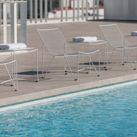 White wire chairs with minimalist design beside a sparkling blue pool, featuring soft white towels on each seat.