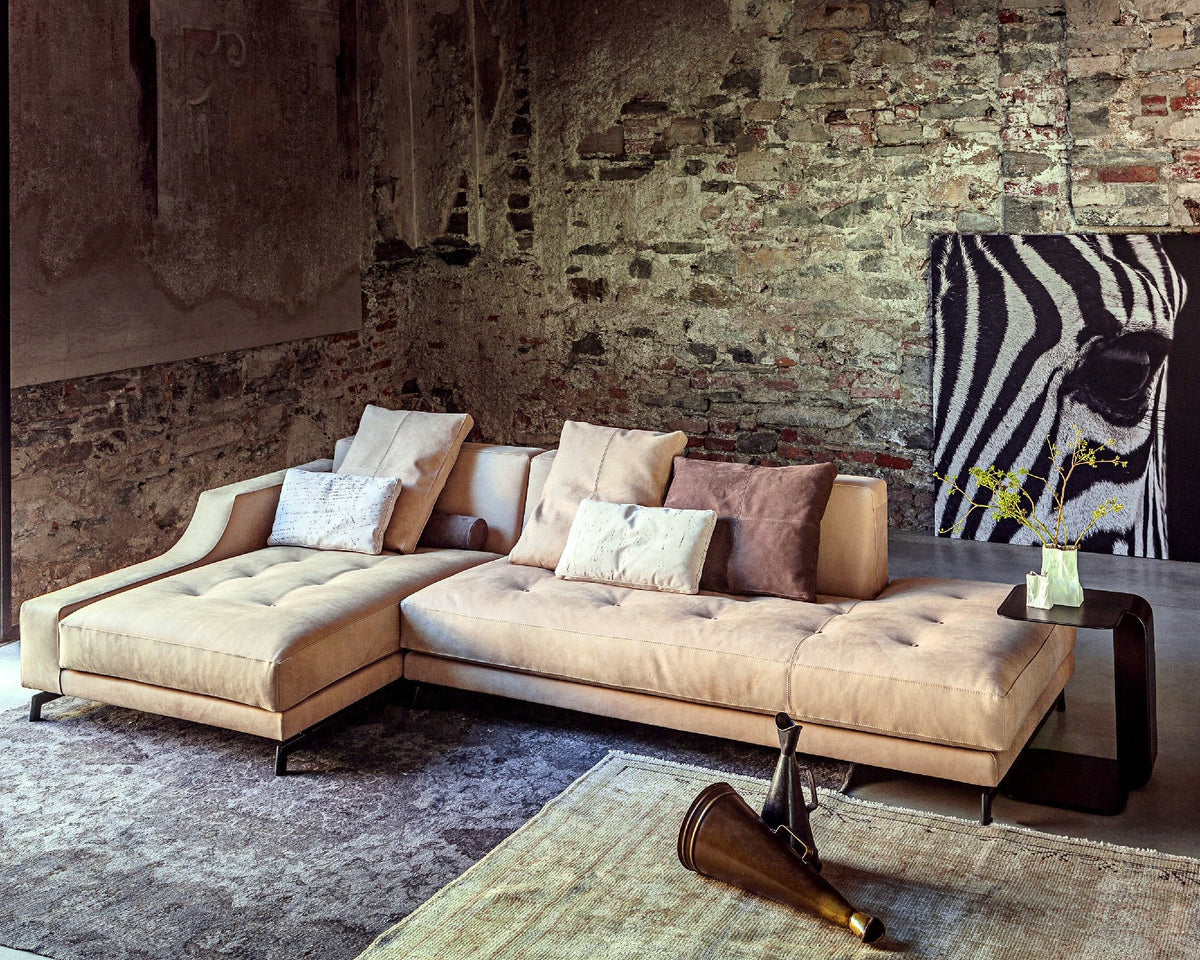 Beige sectional sofa with textured fabric, complemented by neutral and pastel throw pillows, against a rustic brick wall.